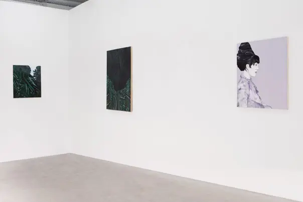 Three paintings displayed on the wall inside a gallery